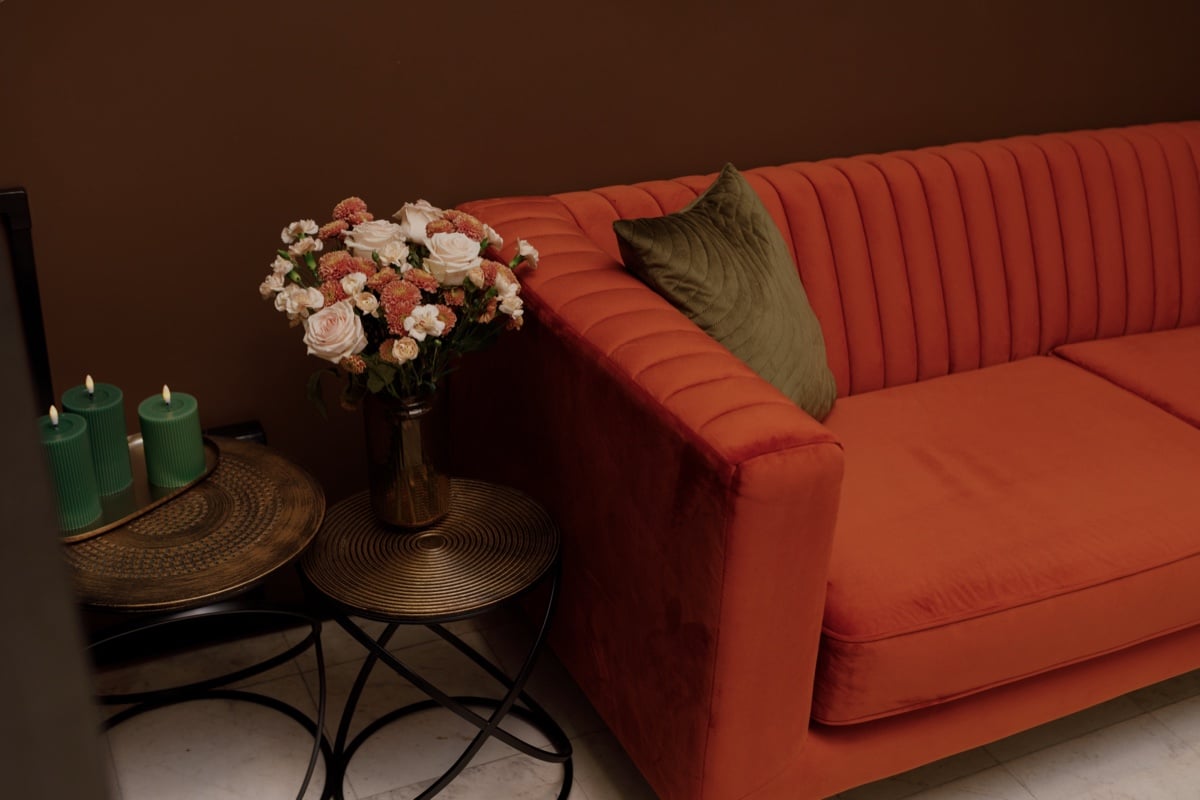 Kącik wypoczynkowy: aksamitna sofa, bukiet róż i zielone świece na mosiężnych stolikach