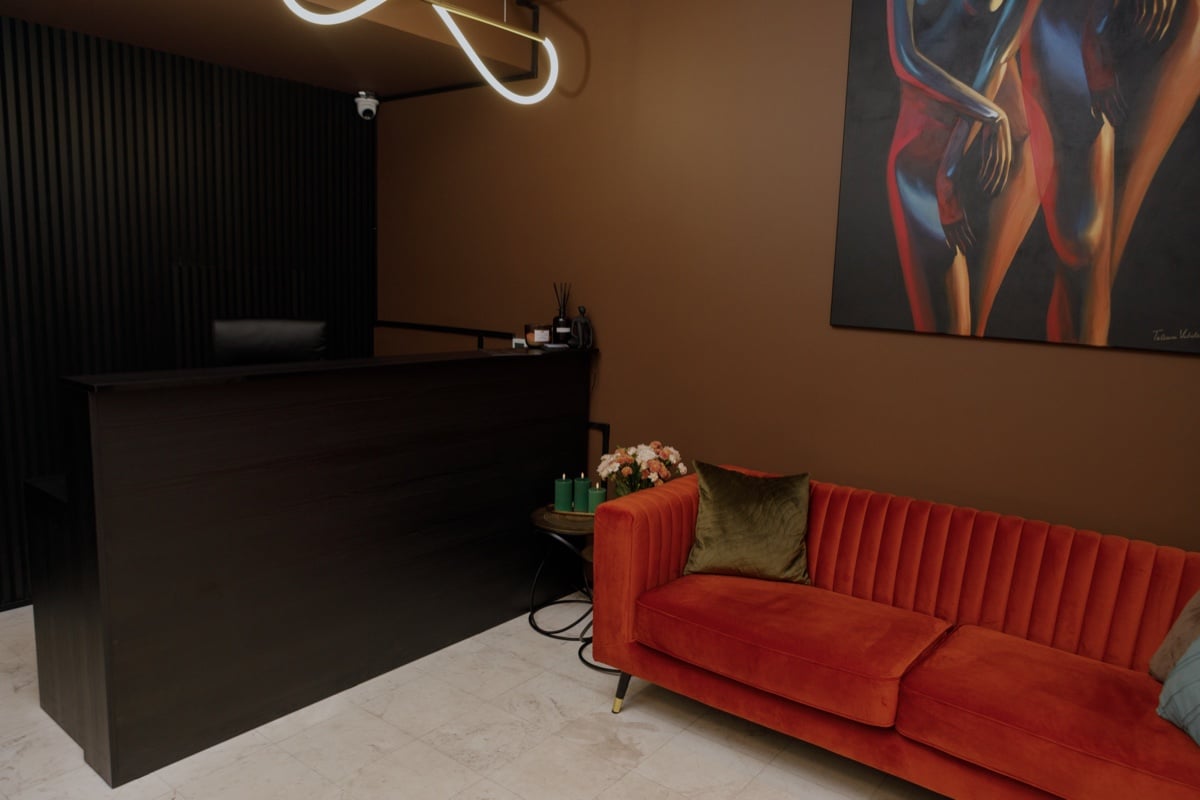 Recepcja UTOPIA: ciemna lada, pomarańczowa aksamitna sofa i neonowa lampa pod sufitem